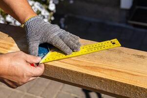 Yellow ruler placed on a wooden beam. Tools are being used to measure and mark the wooden beam for cutting or construction. The close-up view of the tools and the wooden beam. photo