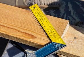 Yellow ruler placed on a wooden beam. Tools are being used to measure and mark the wooden beam for cutting or construction. The close-up view of the tools and the wooden beam. photo