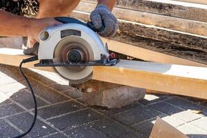 Carpenter is using a circular saw to cut a piece of wood in his workshop. He is wearing protective gear and is using the saw safely photo
