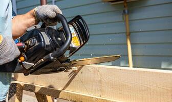 The handyman was sawing at the tree, Indonesia, March 9, 2024 workers are sawing trees, the trees are uprooted, then split into planks and wooden beams, with hand chainsaws, the wood is made into buil photo