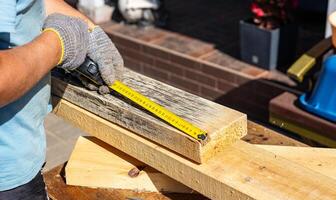 A builder measures a beam with a yellow tape measure. The beam is lying on a table, and the tape measure is extended across it. Step of measuring and cutting materials to create a structure. photo