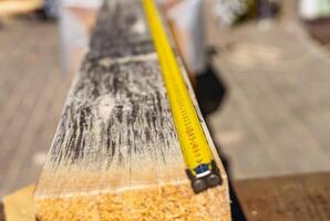 A builder measures a beam with a yellow tape measure. The beam is lying on a table, and the tape measure is extended across it. Step of measuring and cutting materials to create a structure. photo