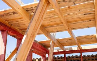 The image shows a close-up view of the wooden beams of a roof structure under construction. The image conveys a sense of progress and anticipation, suggesting that the house is nearing completion. photo