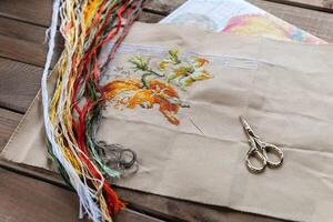 Close-up of a cross-stitch in progress. Cross-stitch with various colorful threads, a needle, and a pair of embroidery scissors. Intricate embroidery details, as well as the sewing process. photo