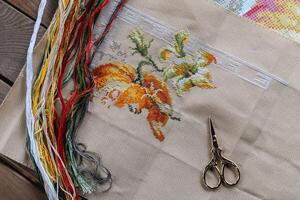 Close-up of a cross-stitch in progress. Cross-stitch with various colorful threads, a needle, and a pair of embroidery scissors. Intricate embroidery details, as well as the sewing process. photo