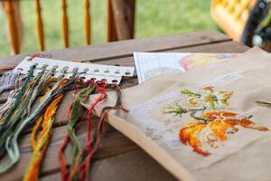 Close-up of a cross-stitch in progress. Cross-stitch with various colorful threads, a needle, and a pair of embroidery scissors. Intricate embroidery details, as well as the sewing process. photo