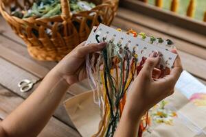 Hand holding a card with numbered slots for different colored embroidery threads. Card and thread are laid out on a wooden surface, suggesting a craft setting. Embroidery. photo