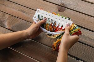 Hand holding a card with numbered slots for different colored embroidery threads. Card and thread are laid out on a wooden surface, suggesting a craft setting. Embroidery. photo