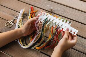 Hand holding a card with numbered slots for different colored embroidery threads. Card and thread are laid out on a wooden surface, suggesting a craft setting. Embroidery. photo