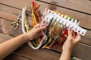 Hand holding a card with numbered slots for different colored embroidery threads. Card and thread are laid out on a wooden surface, suggesting a craft setting. Embroidery. photo