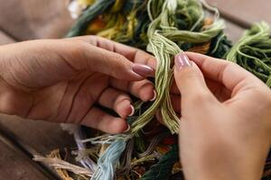 Close-up of hands sorting through a pile of embroidery floss. A large number of multi-colored embroidery threads lie on the table. A girl cross-stitches. Creativity and needlework. photo