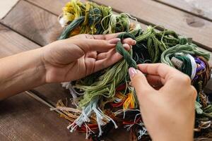 Close-up of hands sorting through a pile of embroidery floss. A large number of multi-colored embroidery threads lie on the table. A girl cross-stitches. Creativity and needlework. photo