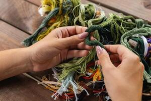 Close-up of hands sorting through a pile of embroidery floss. A large number of multi-colored embroidery threads lie on the table. A girl cross-stitches. Creativity and needlework. photo