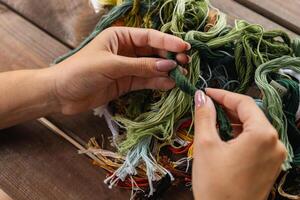 Close-up of hands sorting through a pile of embroidery floss. A large number of multi-colored embroidery threads lie on the table. A girl cross-stitches. Creativity and needlework. photo
