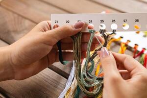 Close-up of hands sorting through a pile of embroidery floss. A large number of multi-colored embroidery threads lie on the table. A girl cross-stitches. Creativity and needlework. photo