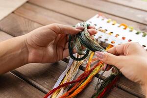 Close-up of hands sorting through a pile of embroidery floss. A large number of multi-colored embroidery threads lie on the table. A girl cross-stitches. Creativity and needlework. photo
