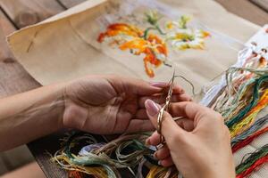 A hand holding embroidery scissors about to cut a thread. A hand with scissors cuts the thread. Close-up of cross stitch. Crafts and embroidery. photo