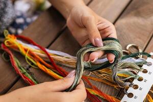 Close-up of hands sorting through a pile of embroidery floss. A large number of multi-colored embroidery threads lie on the table. A girl cross-stitches. Creativity and needlework. photo