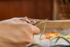 A hand holding embroidery scissors about to cut a thread. A hand with scissors cuts the thread. Close-up of cross stitch. Crafts and embroidery. photo