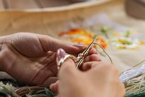 A hand holding embroidery scissors about to cut a thread. A hand with scissors cuts the thread. Close-up of cross stitch. Crafts and embroidery. photo