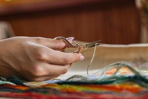 A hand holding embroidery scissors about to cut a thread. A hand with scissors cuts the thread. Close-up of cross stitch. Crafts and embroidery. photo