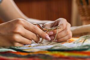 A hand holding embroidery scissors about to cut a thread. A hand with scissors cuts the thread. Close-up of cross stitch. Crafts and embroidery. photo