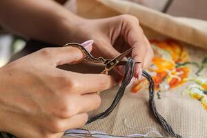 A hand holding embroidery scissors about to cut a thread. A hand with scissors cuts the thread. Close-up of cross stitch. Crafts and embroidery. photo