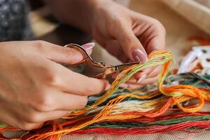 A hand holding embroidery scissors about to cut a thread. A hand with scissors cuts the thread. Close-up of cross stitch. Crafts and embroidery. photo