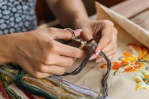 A hand holding embroidery scissors about to cut a thread. A hand with scissors cuts the thread. Close-up of cross stitch. Crafts and embroidery. photo