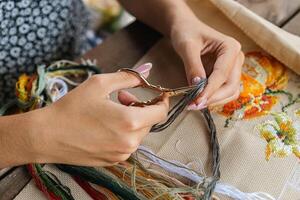A hand holding embroidery scissors about to cut a thread. A hand with scissors cuts the thread. Close-up of cross stitch. Crafts and embroidery. photo