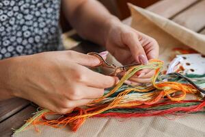A hand holding embroidery scissors about to cut a thread. A hand with scissors cuts the thread. Close-up of cross stitch. Crafts and embroidery. photo