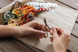 A girl holds needlework scissors in front of threads and embroidery fabric. Crafts and creativity. Cross stitch. photo