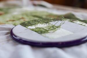 Close-up of a cross-stitch embroidery project in progress. The needle is threaded with green floss and is partially inserted in the fabric. The hoop is purple, and the fabric is white. photo