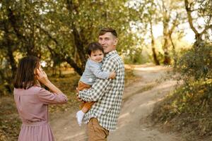 Happy family walking on the road in the park. Father, mother holding baby son on hands and going together. Rear view. Family Ties concept. photo
