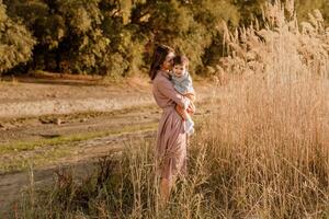 Portrait of happy loving mother hugging her baby son in the sunny park near river photo