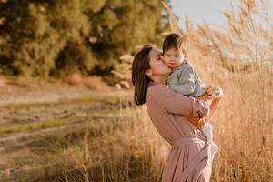 Portrait of happy loving mother hugging her baby son in the sunny park near river photo