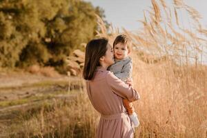 Portrait of happy loving mother hugging her baby son in the sunny park near river photo