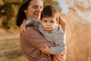 Portrait of happy loving mother hugging her baby son in the sunny park near river photo