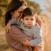 Portrait of happy loving mother hugging her baby son in the sunny park near river photo