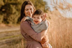 Portrait of happy loving mother hugging her baby son in the sunny park near river photo