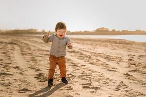 A one-year-old boy learns to walk in the sand by the river photo