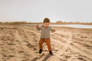 A one-year-old boy learns to walk in the sand by the river photo