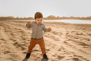 A one-year-old boy learns to walk in the sand by the river photo