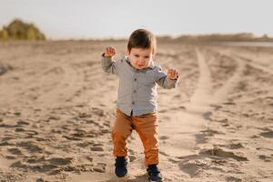A one-year-old boy learns to walk in the sand by the river photo