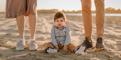 One year old boy with mom and dad sitting on the river bank and playing with sand photo