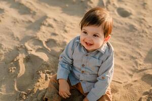 One-year-old boy sitting in the sand, smiling and playing photo