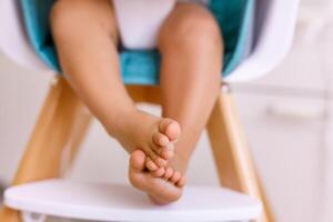 One years old child's feet on high chair while he is eating at kitchen dinner table. photo