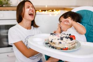 Happy mother with one year old baby celebrating with first birthday with white kitchen on background photo