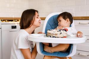 Happy mother with one year old baby celebrating with first birthday with white kitchen on background photo
