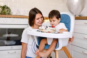 Happy mother with one year old baby celebrating with first birthday with white kitchen on background photo